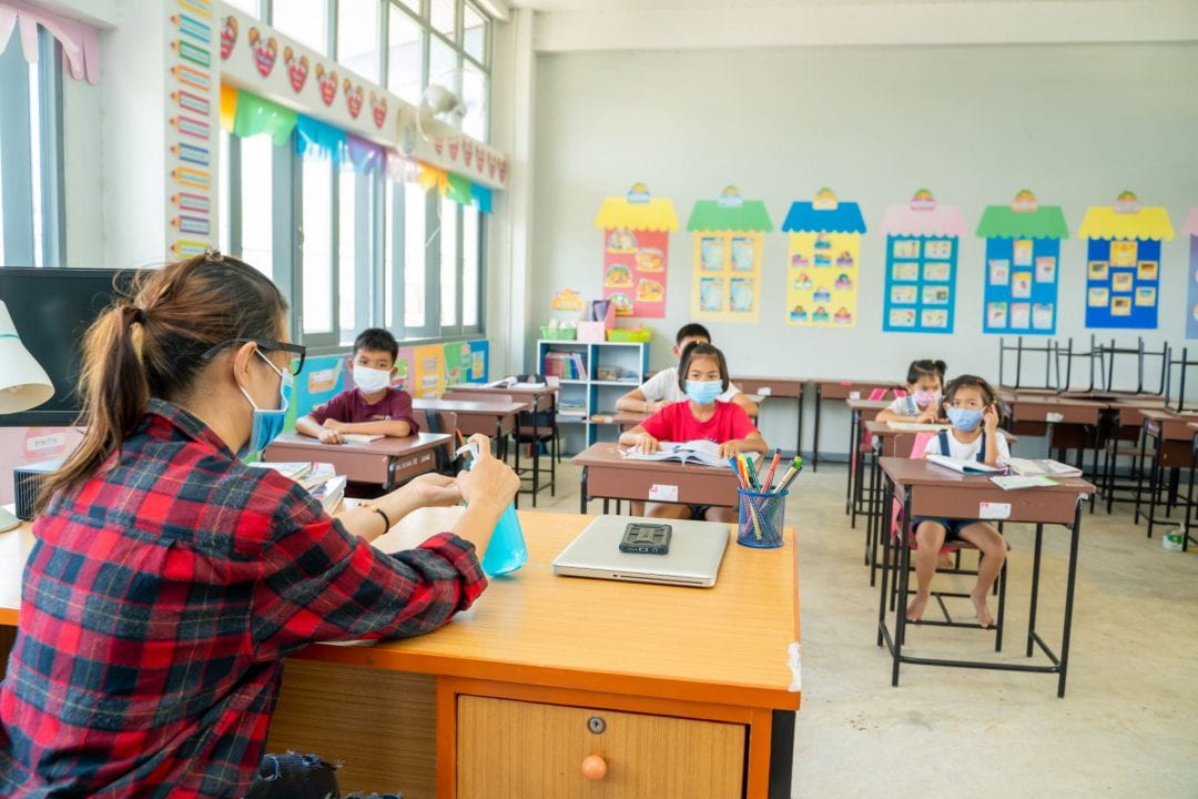 An elementary classroom with students and teacher wearing a mask.